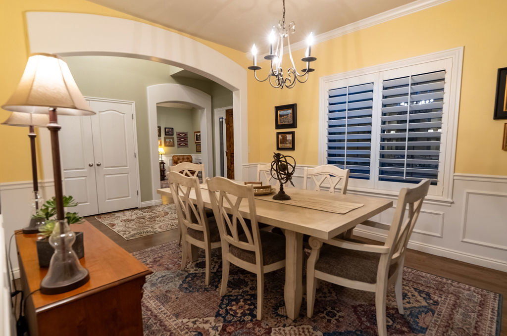Dining area featuring bright yellow walls with white wainscoting, a chandelier, and a window with white louvered shutters