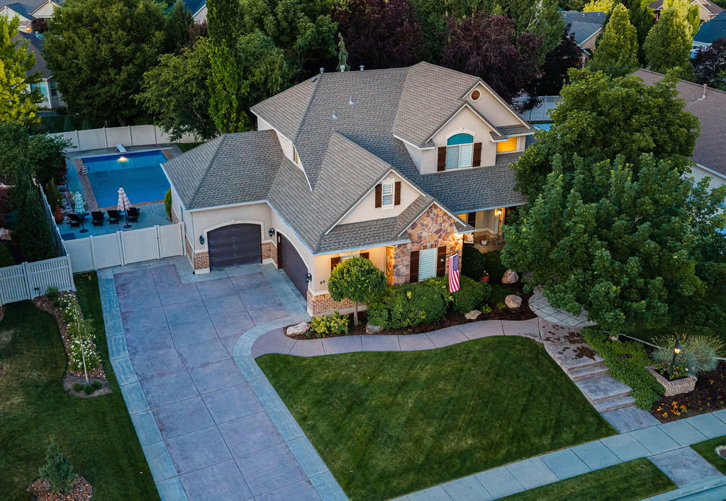Stucco and stone facade property featuring an attached two-car garage, mature landscaping, and a fenced backyard swimming pool