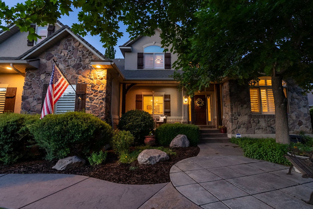 Stone facade home featuring mature landscaping, a concrete paver walkway, plantation shutters, and a covered entryway with an ornate front door