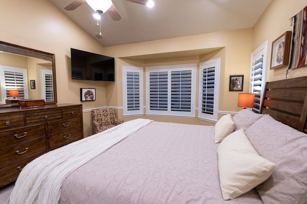 Spacious room featuring a bay window with plantation shutters, vaulted ceiling, and ceiling fan