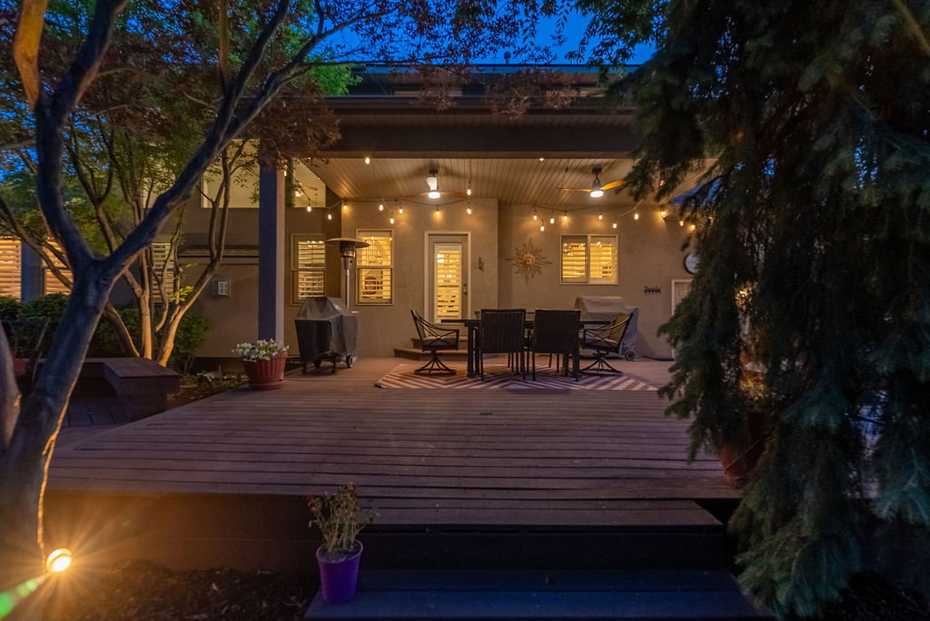 Spacious outdoor wood deck with layered steps, covered patio featuring string lights and two ceiling fans, and integrated exterior lighting