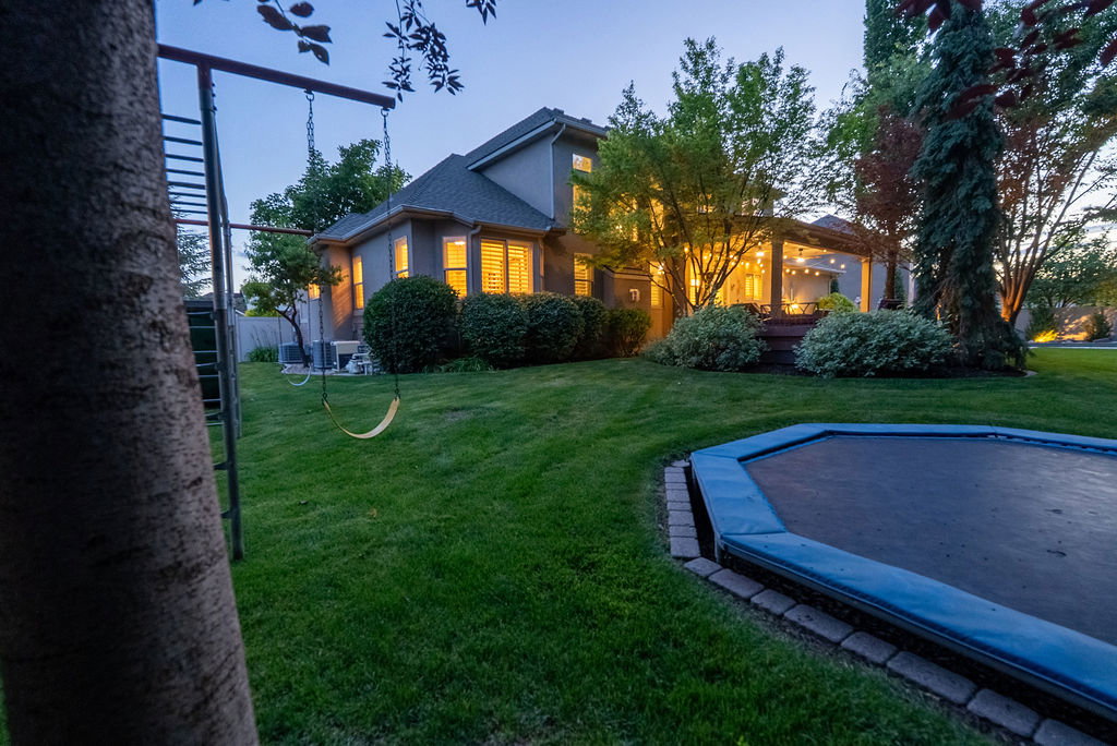 Expansive backyard featuring a manicured lawn, mature trees, and a spacious covered patio with string lighting