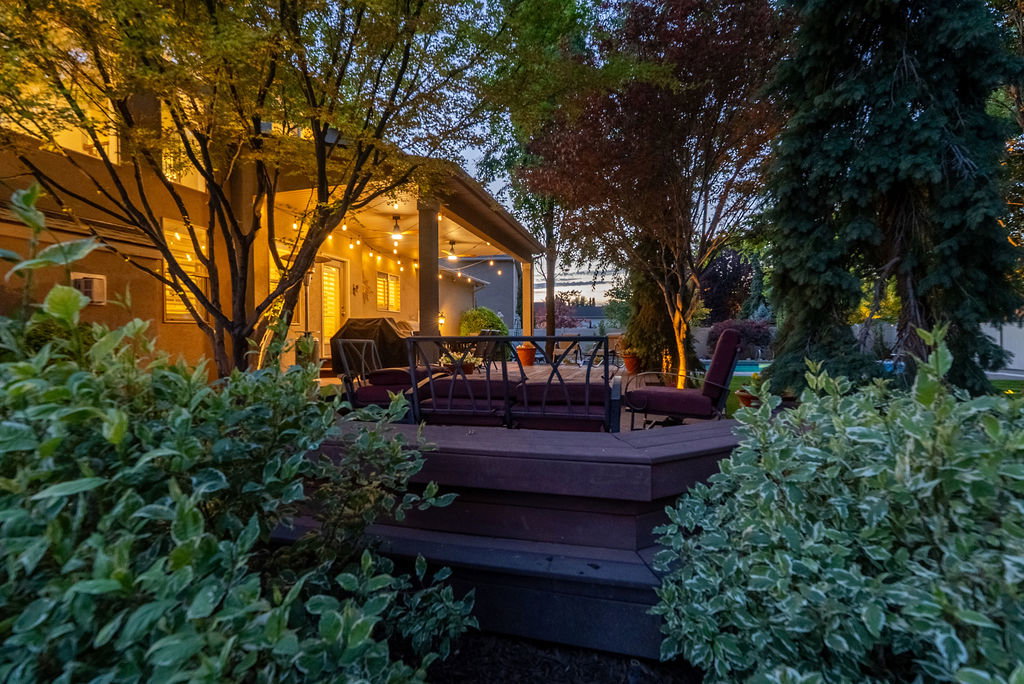 Expansive outdoor area featuring a multi-level wood-finish deck with integrated steps, a covered patio, and mature landscaping