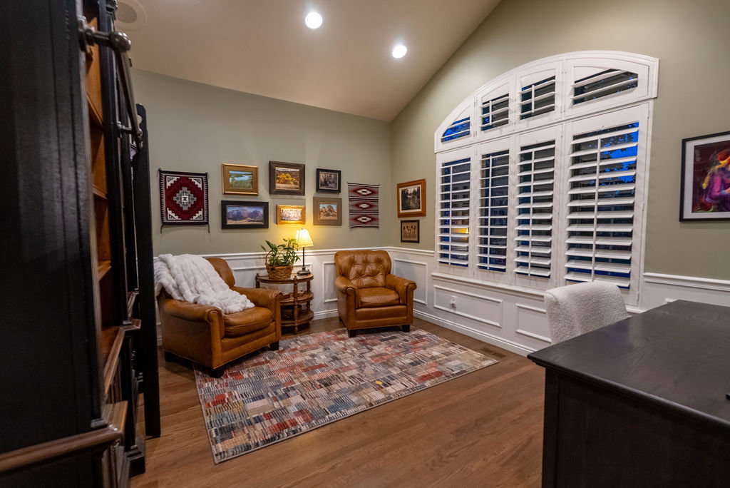 Vaulted ceiling room featuring wood-finish flooring, a large arched window with white plantation shutters, and extensive wainscoting