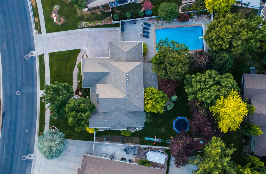 Expansive property featuring a multi-gabled residence, a large rectangular swimming pool with a diving board, a concrete patio area, mature landscaping, and a manicured lawn