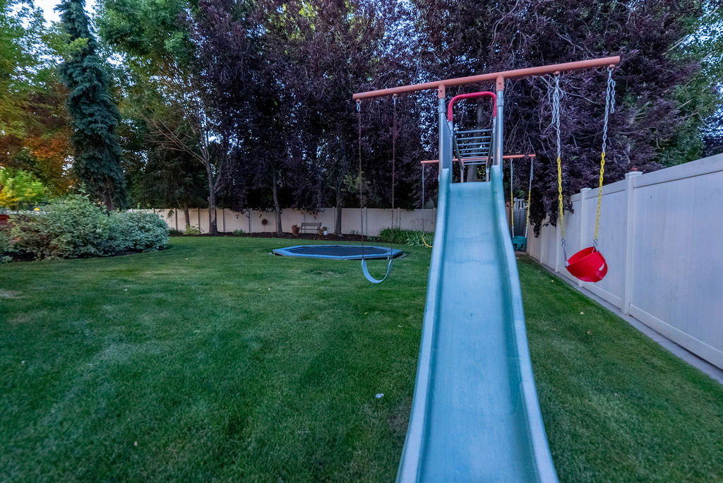 Expansive backyard featuring a lush green lawn, mature perimeter trees, and a white privacy fence