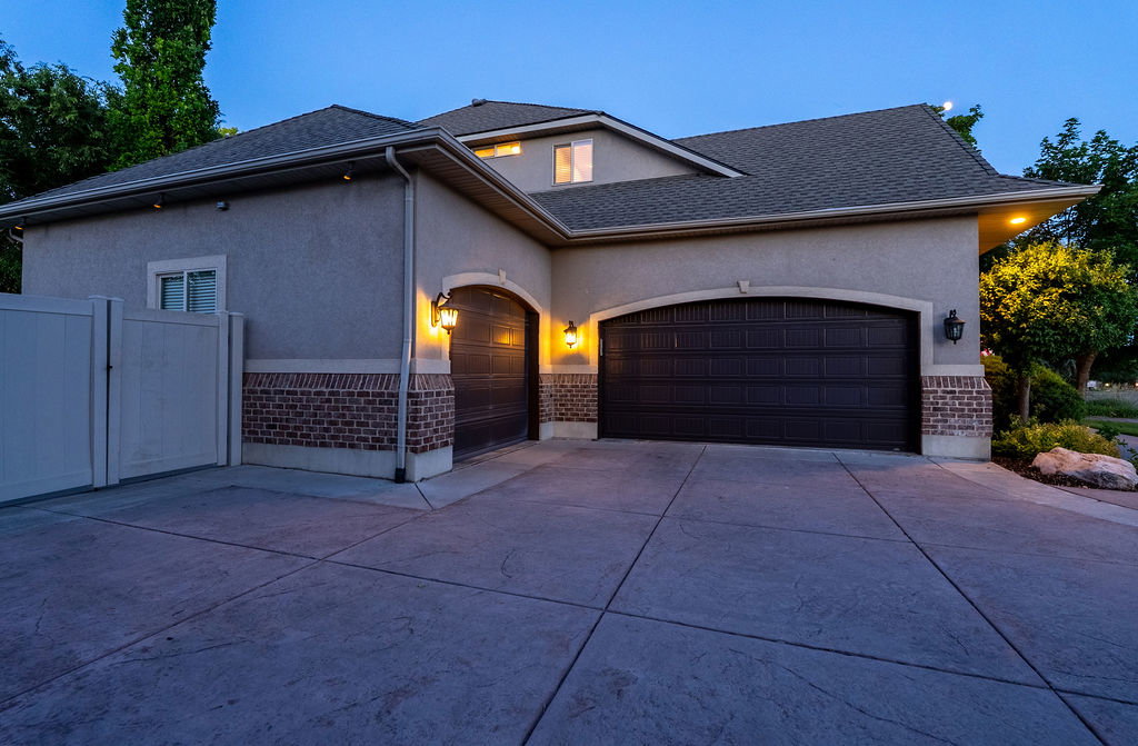 Two-car garage with arched doors and exterior sconce lighting, complemented by a brick veneer base and stucco siding