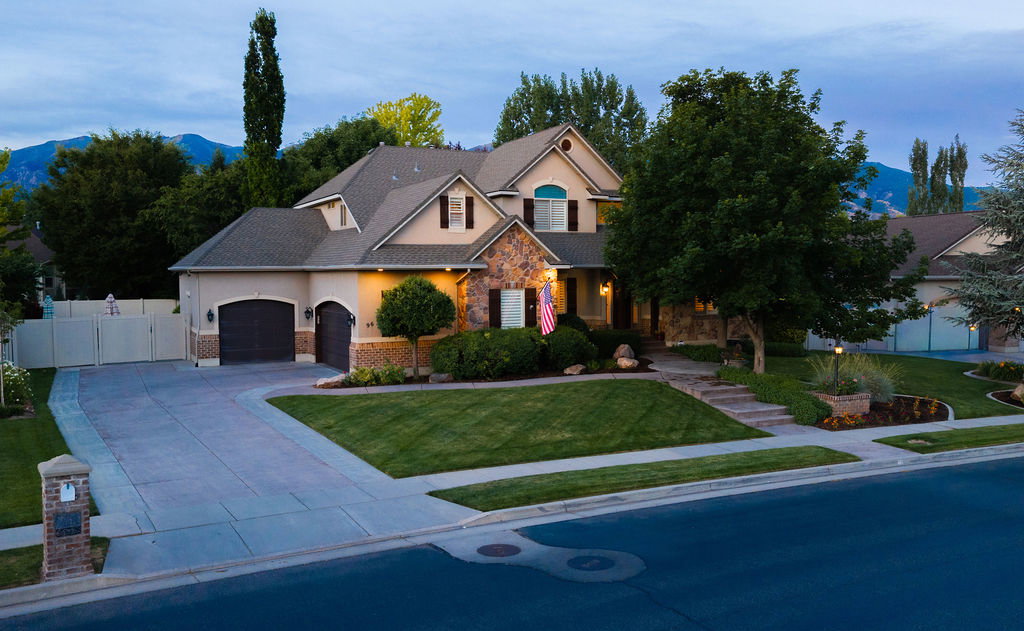 Stucco and stone facade property with a multi-car driveway, a meticulously landscaped front yard, and mature trees