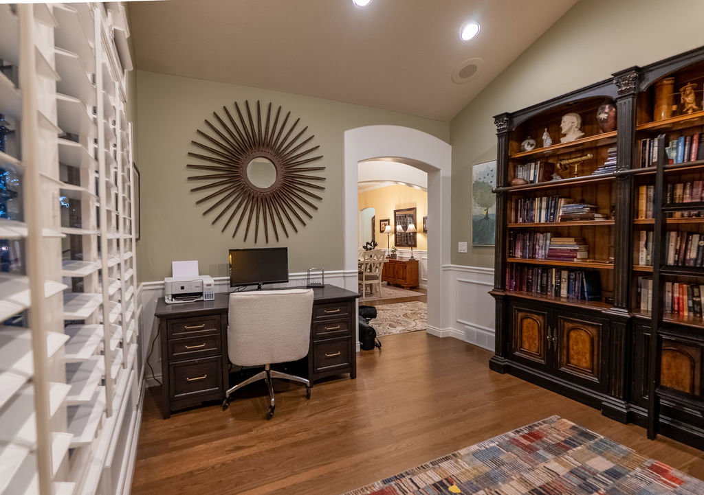 Dedicated office space featuring built-in bookcases, wood-finish flooring, and natural light from plantation-shutter windows