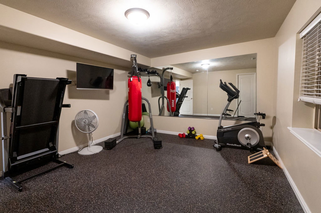 Dedicated exercise space featuring rubberized flooring, a wall-mounted mirror, recessed ceiling lighting, and a window with blinds