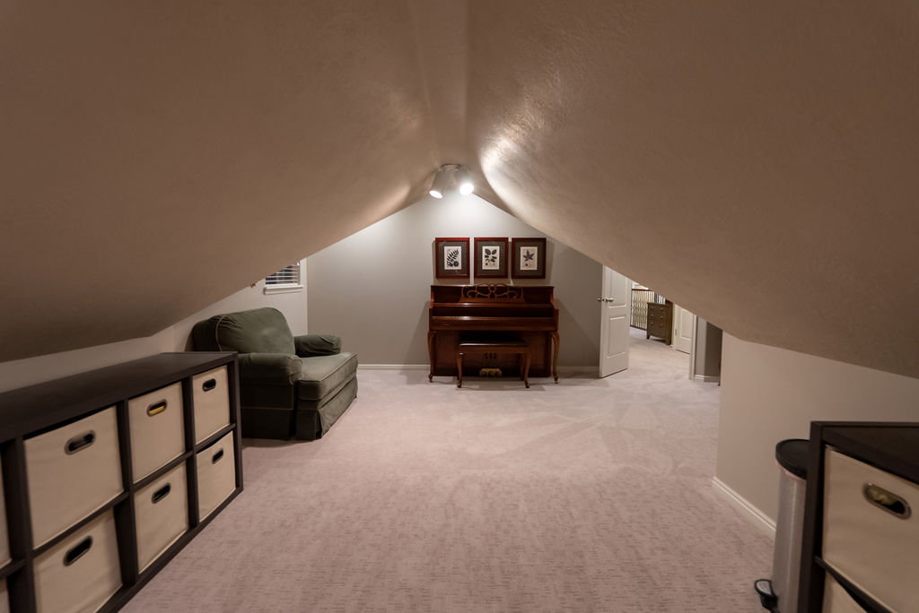 Carpeted attic space featuring sloped ceilings, track lighting, and a white interior door