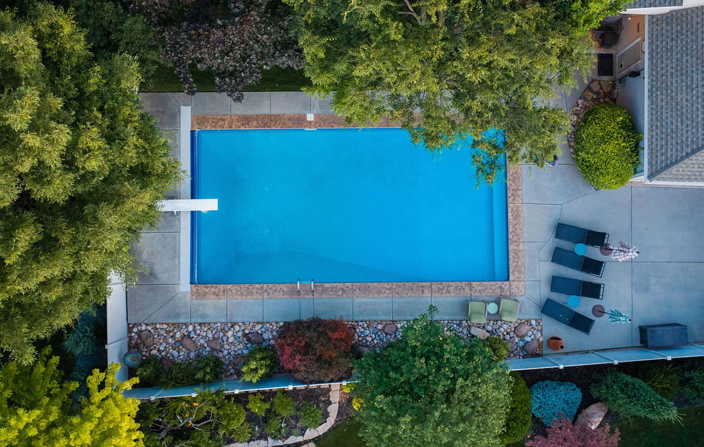 Rectangular swimming pool with a diving board, surrounded by concrete decking and mature trees