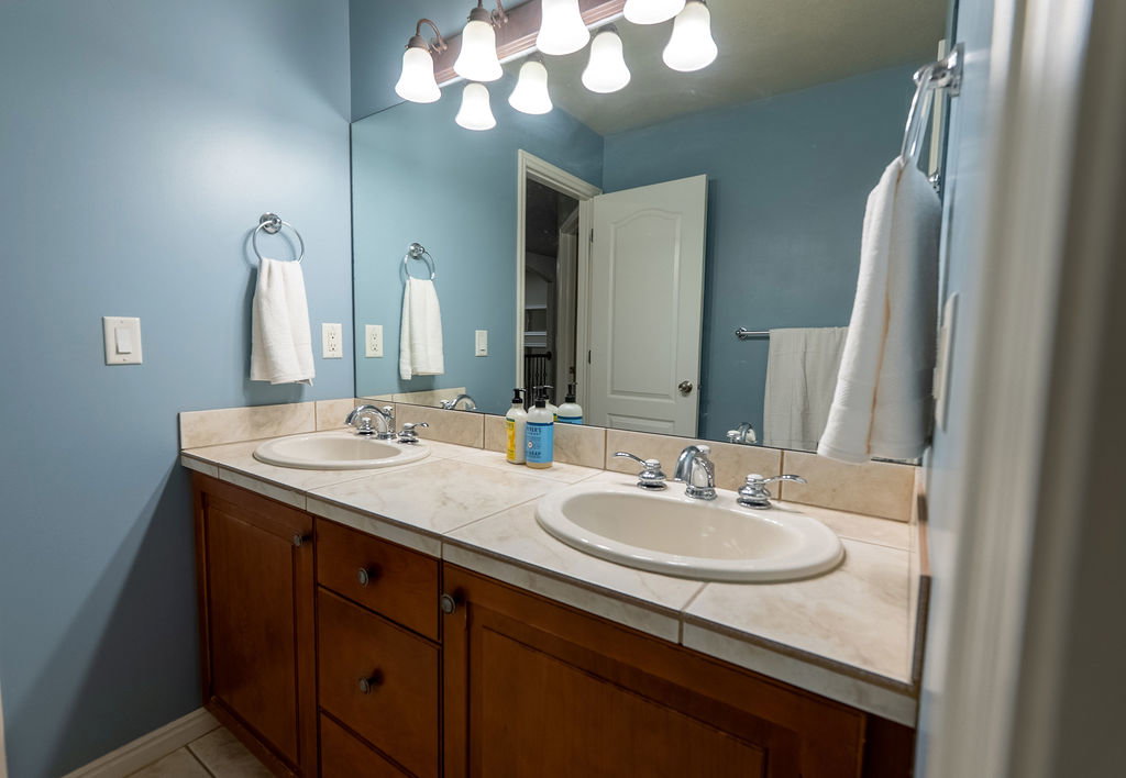 Dual vanity featuring integrated sinks, tile countertop, and wood-finish cabinetry