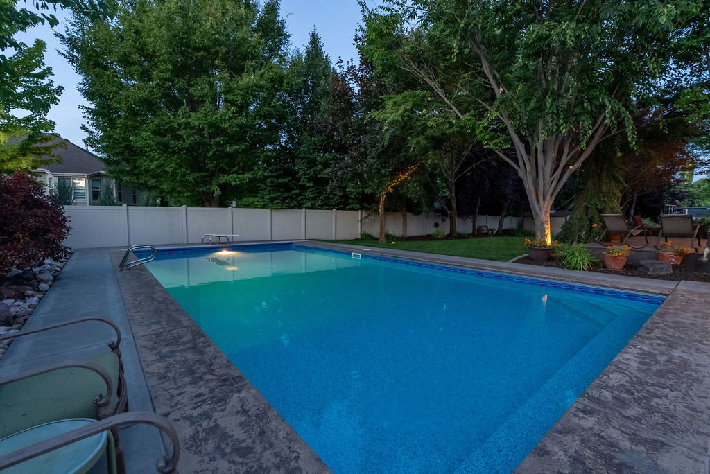 In-ground swimming pool with stamped concrete coping and surround, featuring a surrounding lawn area and mature trees