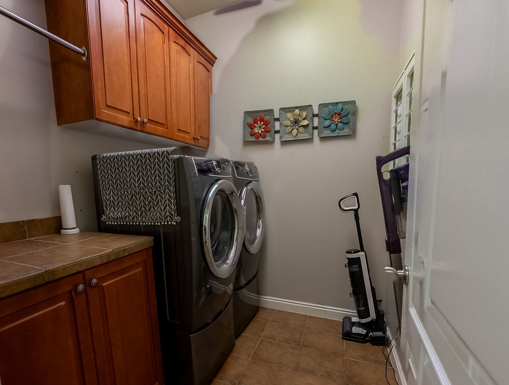 Dedicated laundry area featuring a built-in wood-finish cabinetry, tile flooring, a tile countertop, and an overhead hanging rod