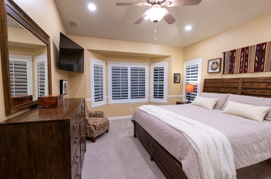 Recessed lighting illuminates this space featuring a ceiling fan, bay window with plantation shutters, and light-toned carpeting