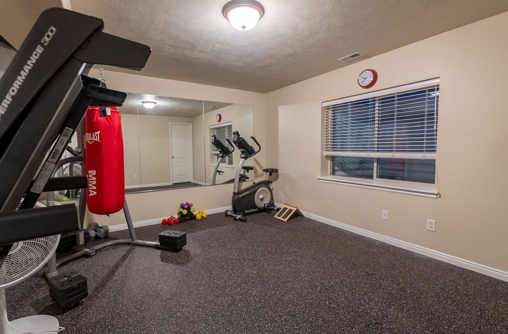 Dedicated fitness space featuring specialized rubberized flooring, a full-wall mirror, and a window with horizontal blinds