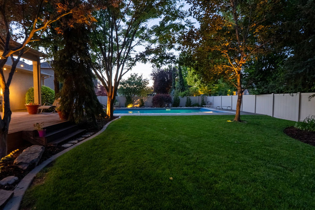 Spacious backyard featuring a manicured lawn, an in-ground swimming pool, and mature trees with landscape lighting