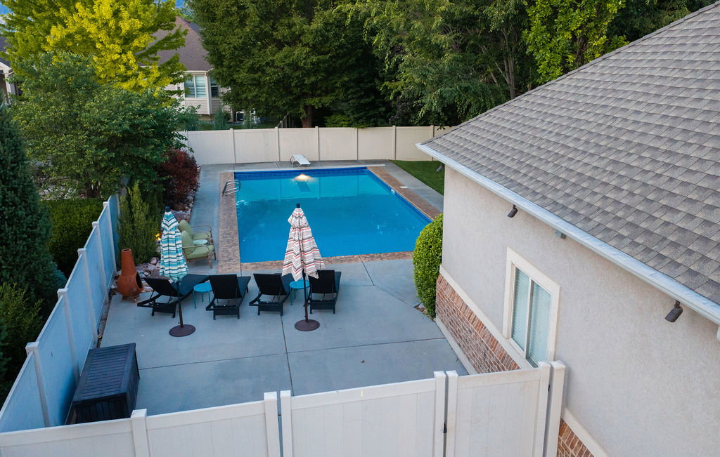 Outdoor concrete patio featuring an in-ground swimming pool, surrounded by a privacy fence and mature landscaping