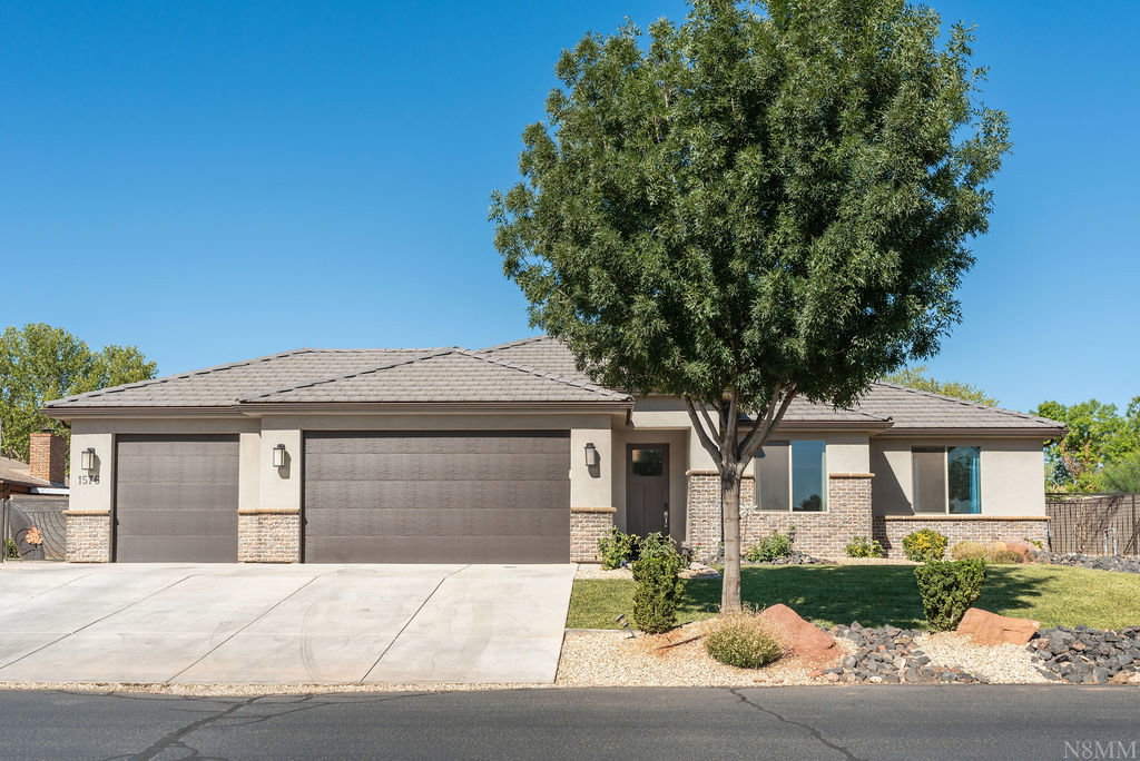 Contemporary stucco exterior featuring a multi-car garage with panel doors, stone accents, and exterior lighting fixtures