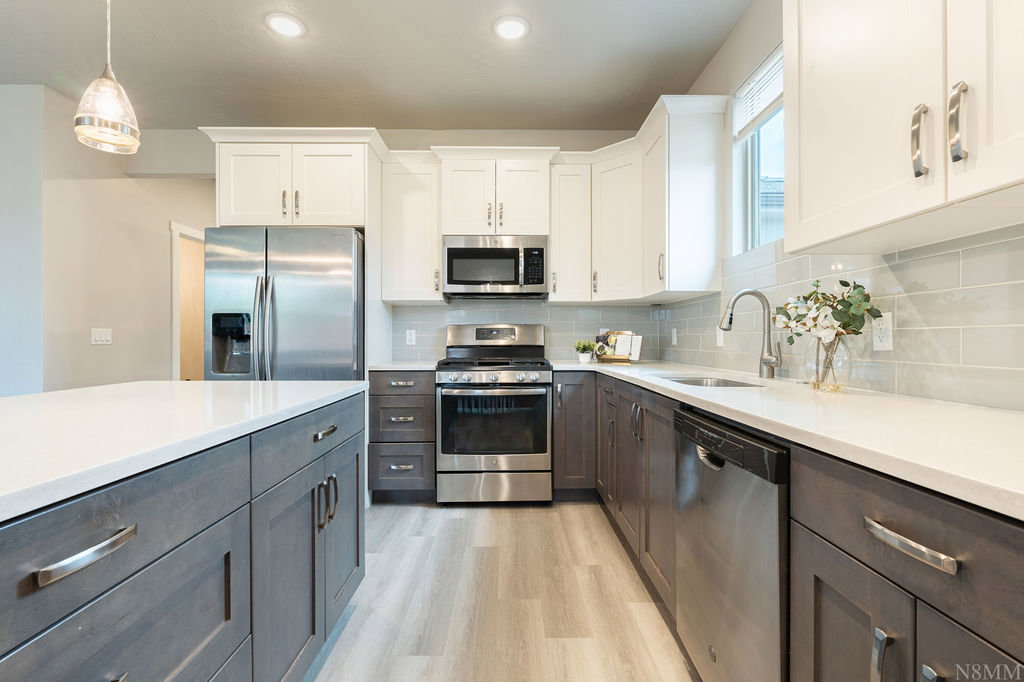 Kitchen featuring a large island with white countertops, stainless steel appliances, two-tone cabinetry, wood-finish flooring, and subway tile backsplash
