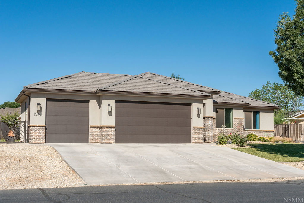Contemporary stucco exterior with stone accents, a tile roof, and a three-car garage