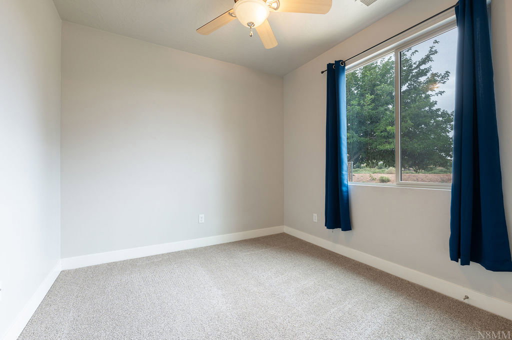 Carpeted room featuring a large window, neutral wall tones, white baseboards, and a ceiling fan with integrated lighting
