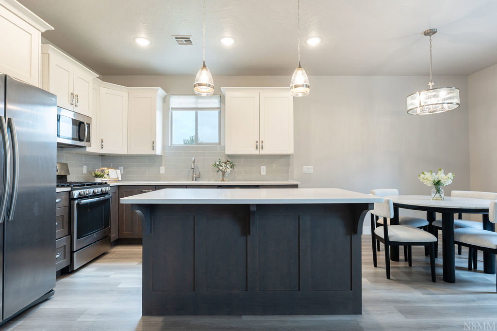 Modern kitchen featuring a central island with a light-toned countertop, stainless steel appliances, two-tone cabinetry, and wood-finish flooring