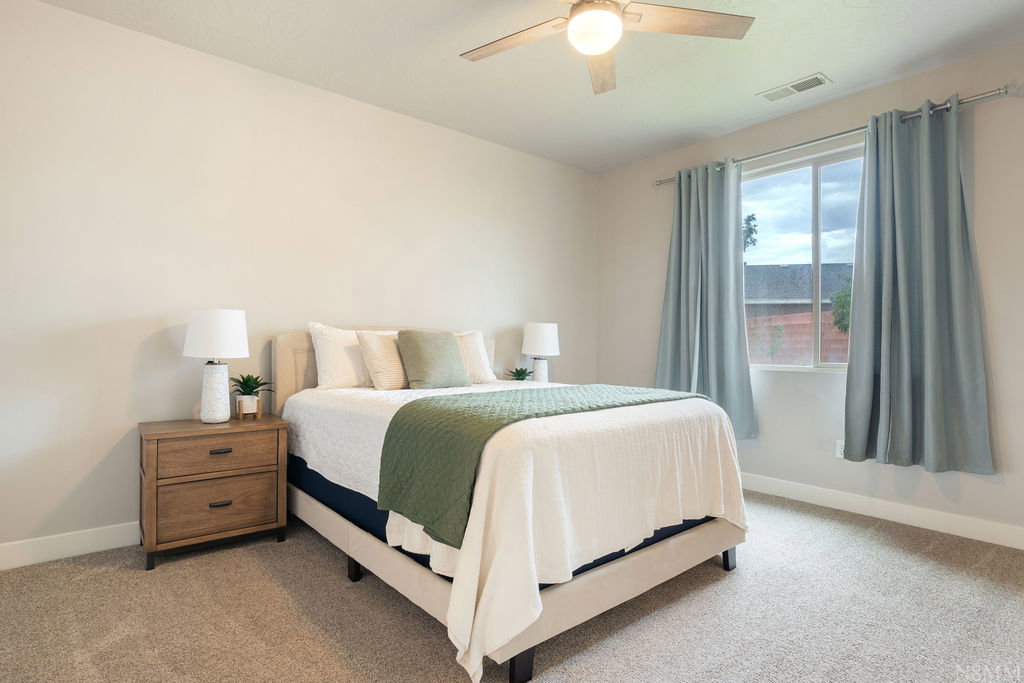 Bright bedroom featuring a double-pane window, neutral carpet flooring, and a ceiling fan with integrated lighting