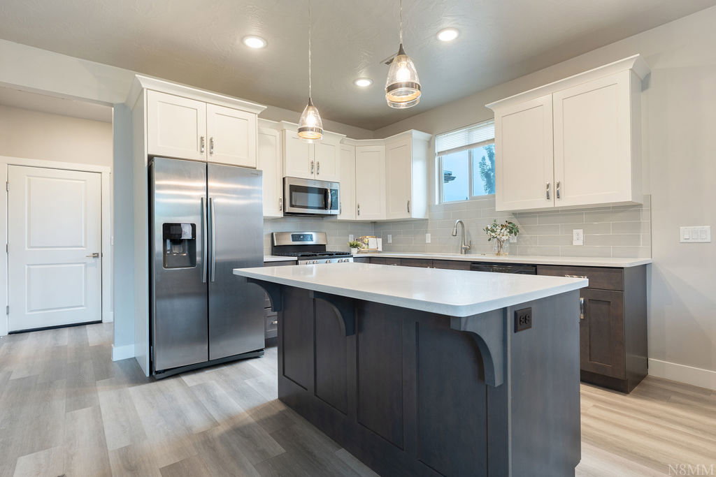 Spacious kitchen featuring an island with a light-colored countertop, stainless steel appliances, two-tone cabinetry, wood-finish flooring, and recessed lighting