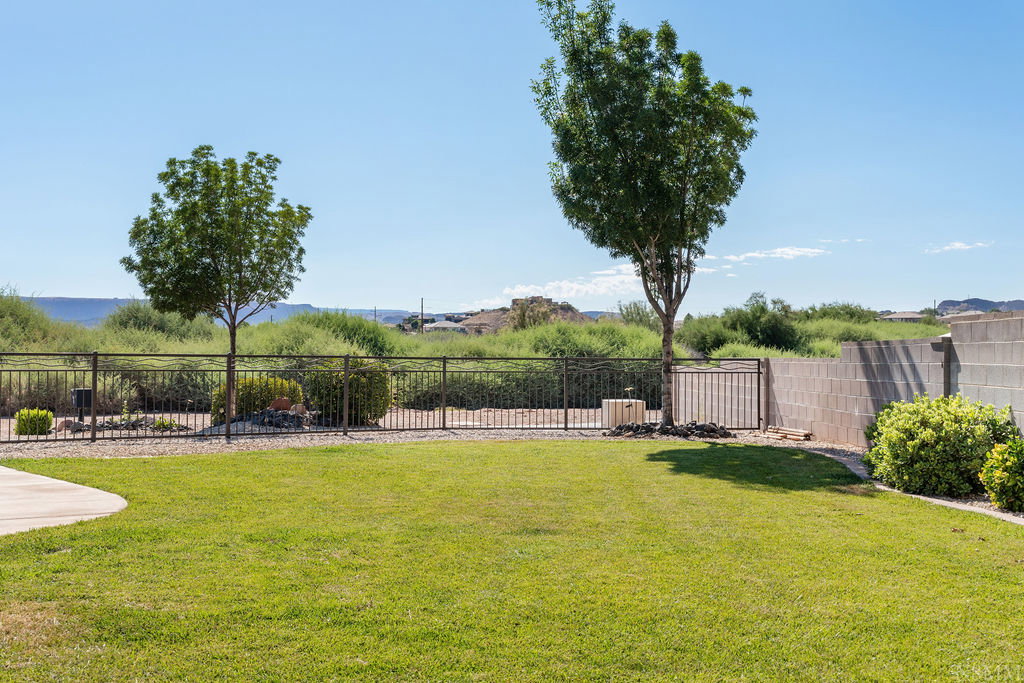 Expansive backyard featuring a lush lawn, mature trees, and a black wrought iron fence