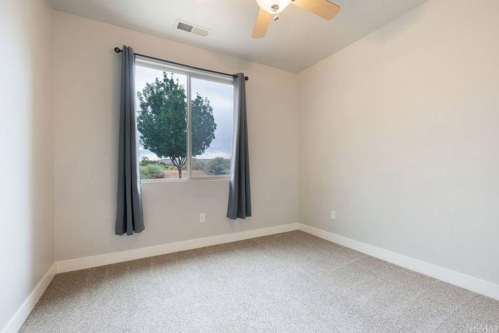 Neutral-toned interior featuring a ceiling fan with light fixture, light gray carpeting, and white baseboards