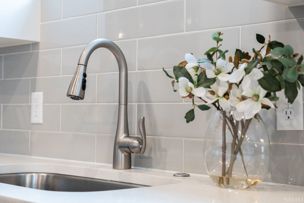 Stainless steel pull-down faucet with a single-basin sink, set against a light grey subway tile backsplash