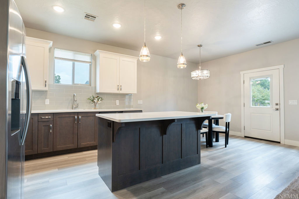 Open-concept kitchen featuring an island with a white countertop, two-tone cabinetry, stainless steel appliances, and wood-finish flooring