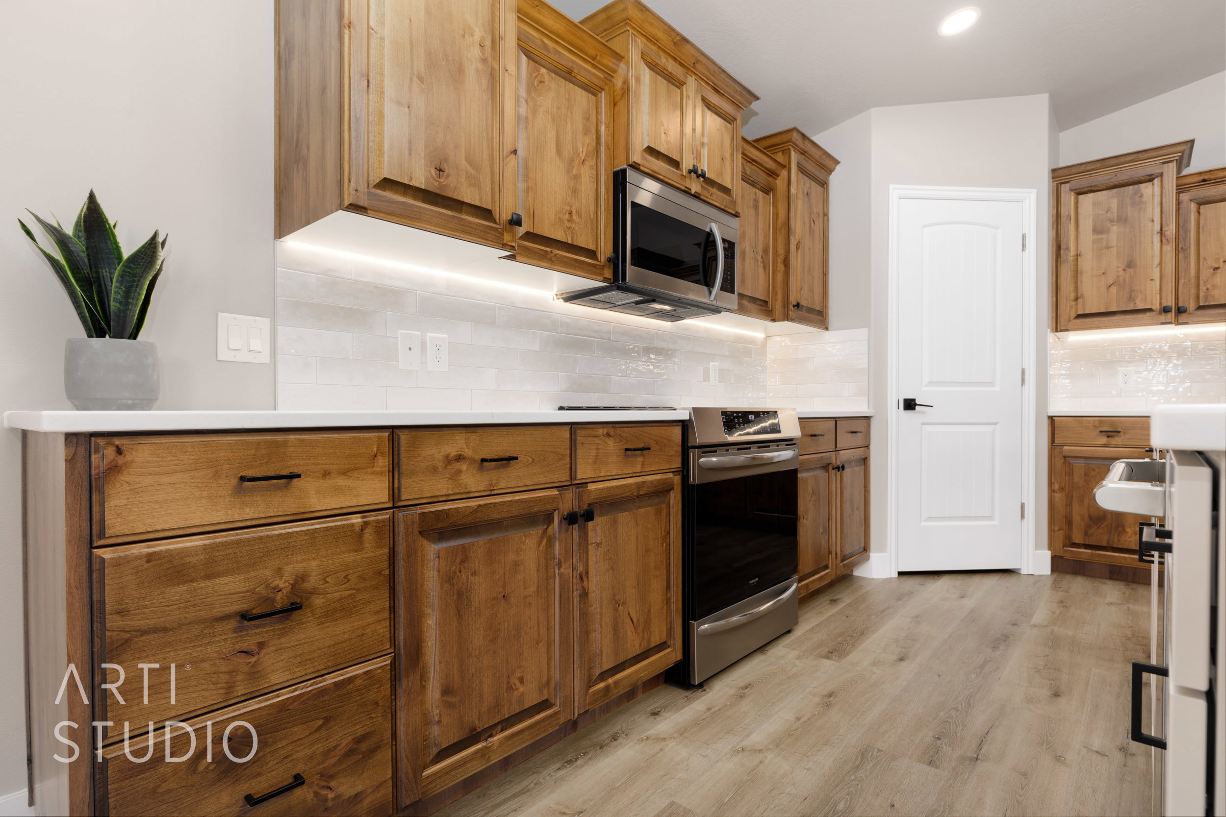 Kitchen featuring wood cabinetry, light-toned countertops, a tile backsplash, stainless steel appliances, and LVP flooring