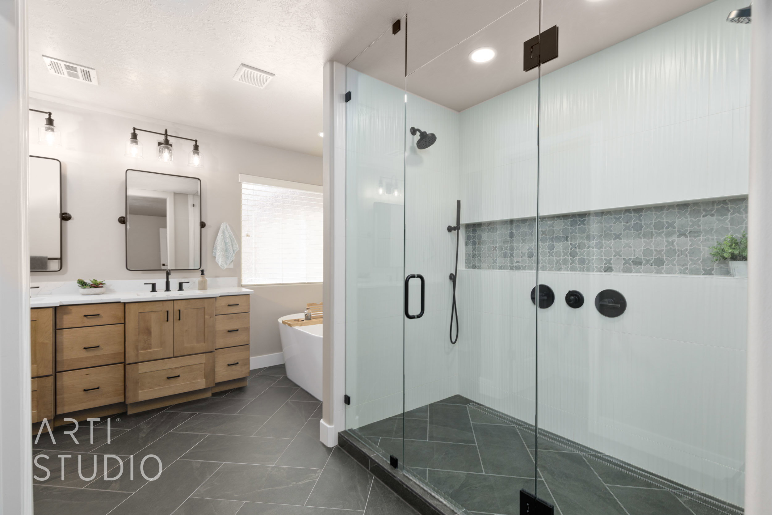 Glass-enclosed shower featuring custom dual shower heads, dark-toned fixtures and a decorative tiled niche