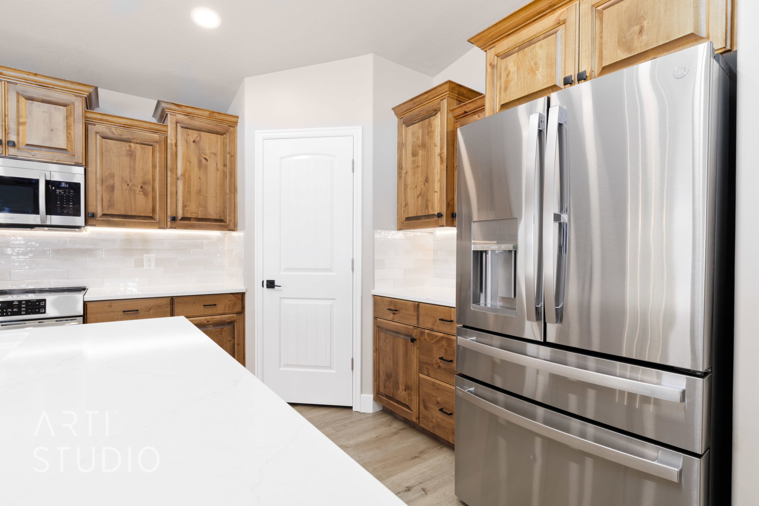 Modern kitchen featuring a stainless steel refrigerator, wood-finish cabinetry, quartz countertops, white subway tile backsplash, and recessed lighting