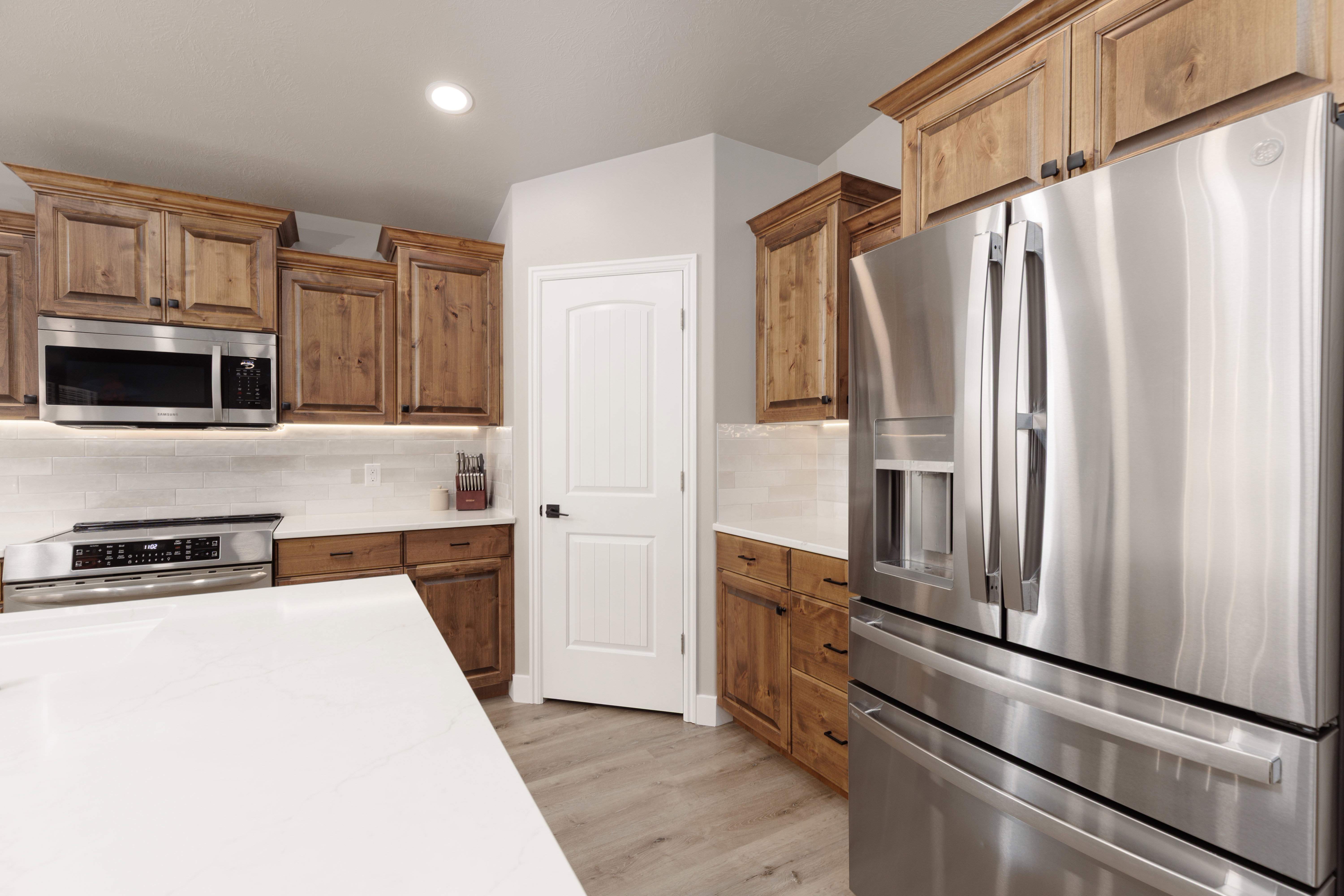 Kitchen featuring wood cabinetry, stainless steel appliances, white subway tile backsplash, white countertops, and LVP flooring