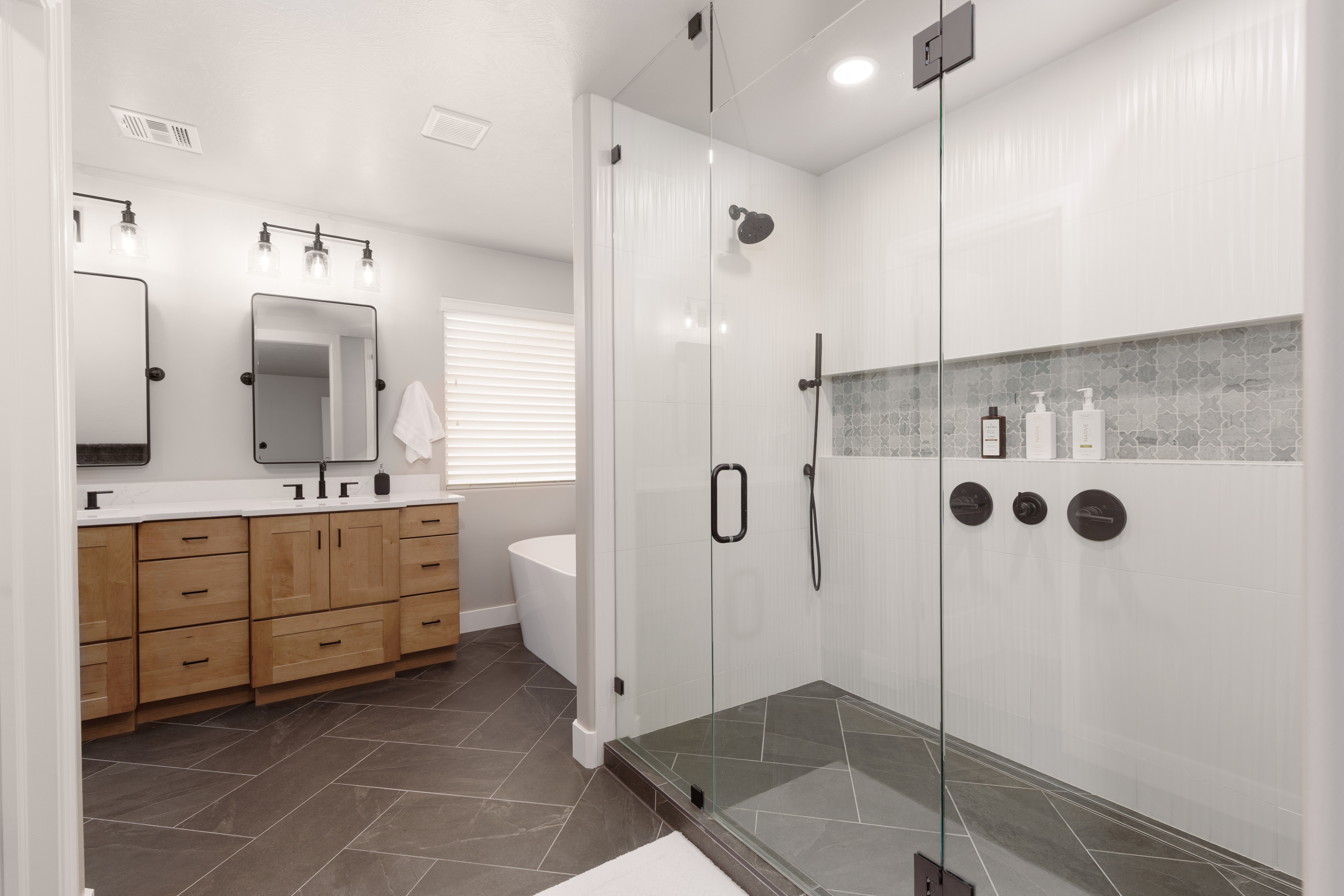 Primary ensuite featuring custom dual shower heads, dark-toned fixtures and a decorative tiled niche