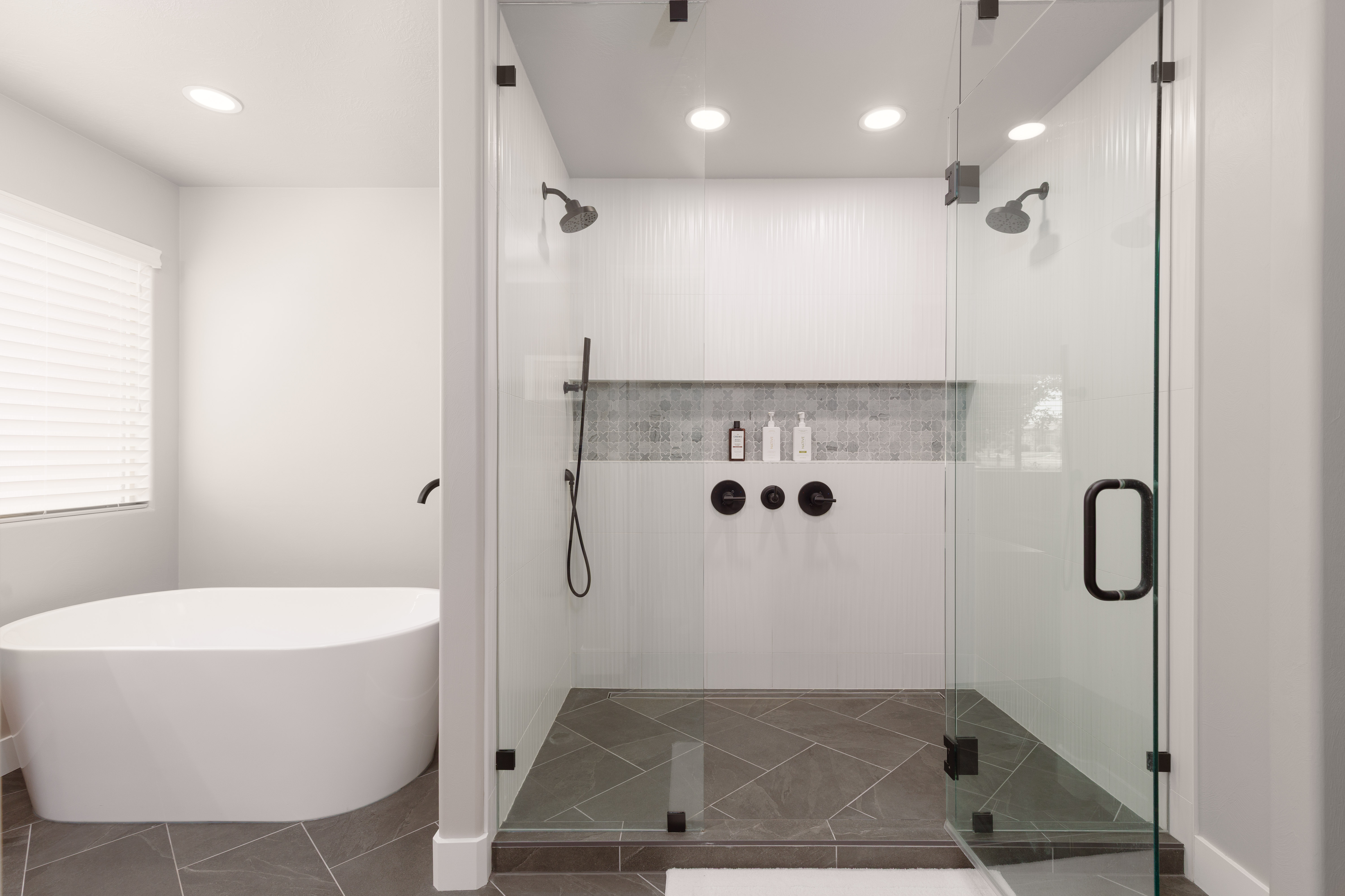Primary ensuite bathroom with custom walk-in glass enclosure shower with dual shower heads large niche and soaking tub