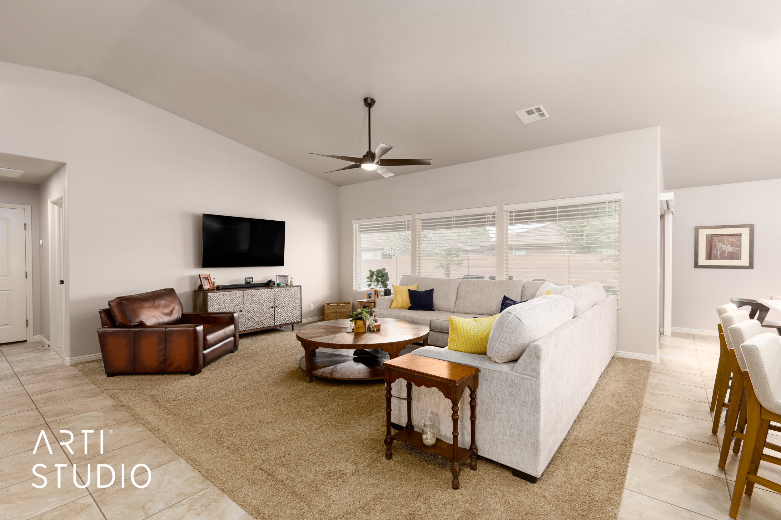 Spacious living area featuring vaulted ceilings, a ceiling fan with integrated lighting, and multiple windows with horizontal blinds