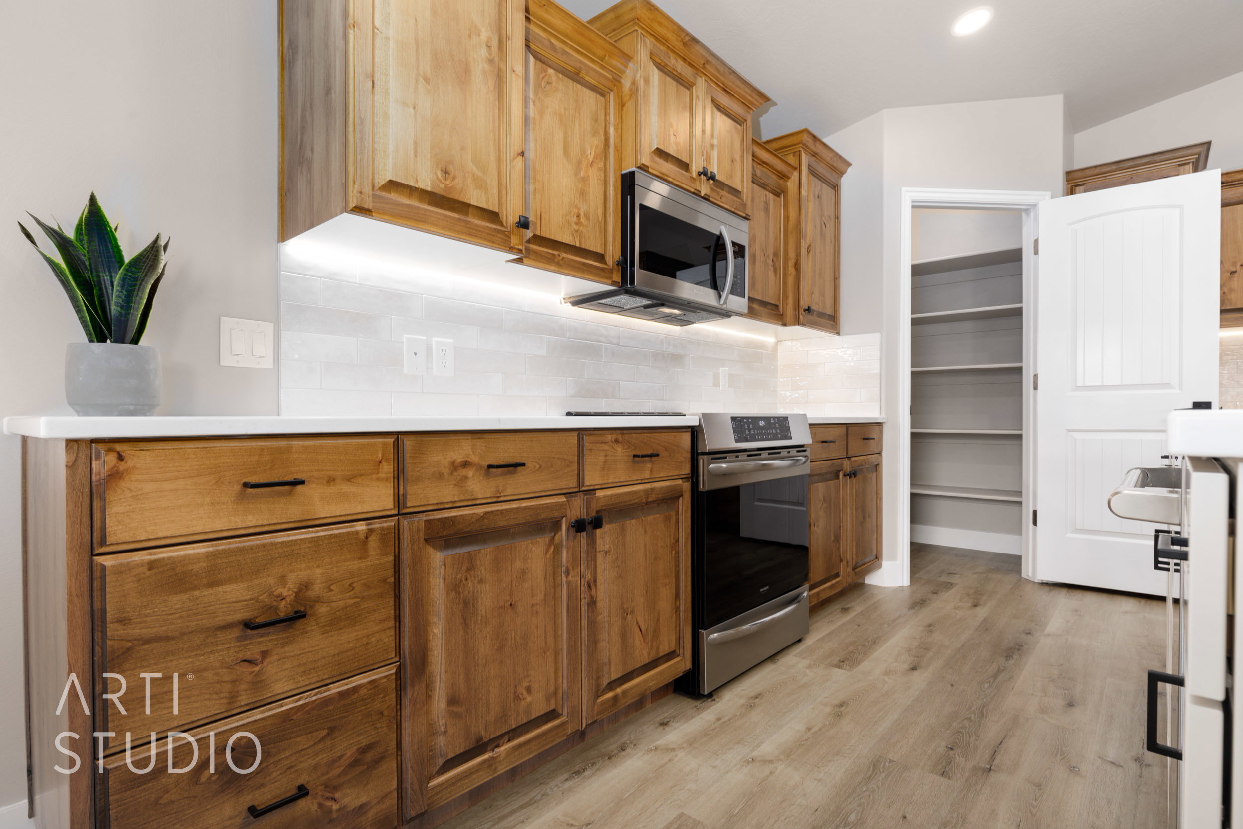 Kitchen featuring wood cabinetry, stainless steel appliances, white subway tile backsplash, white countertops, and LVP flooring
