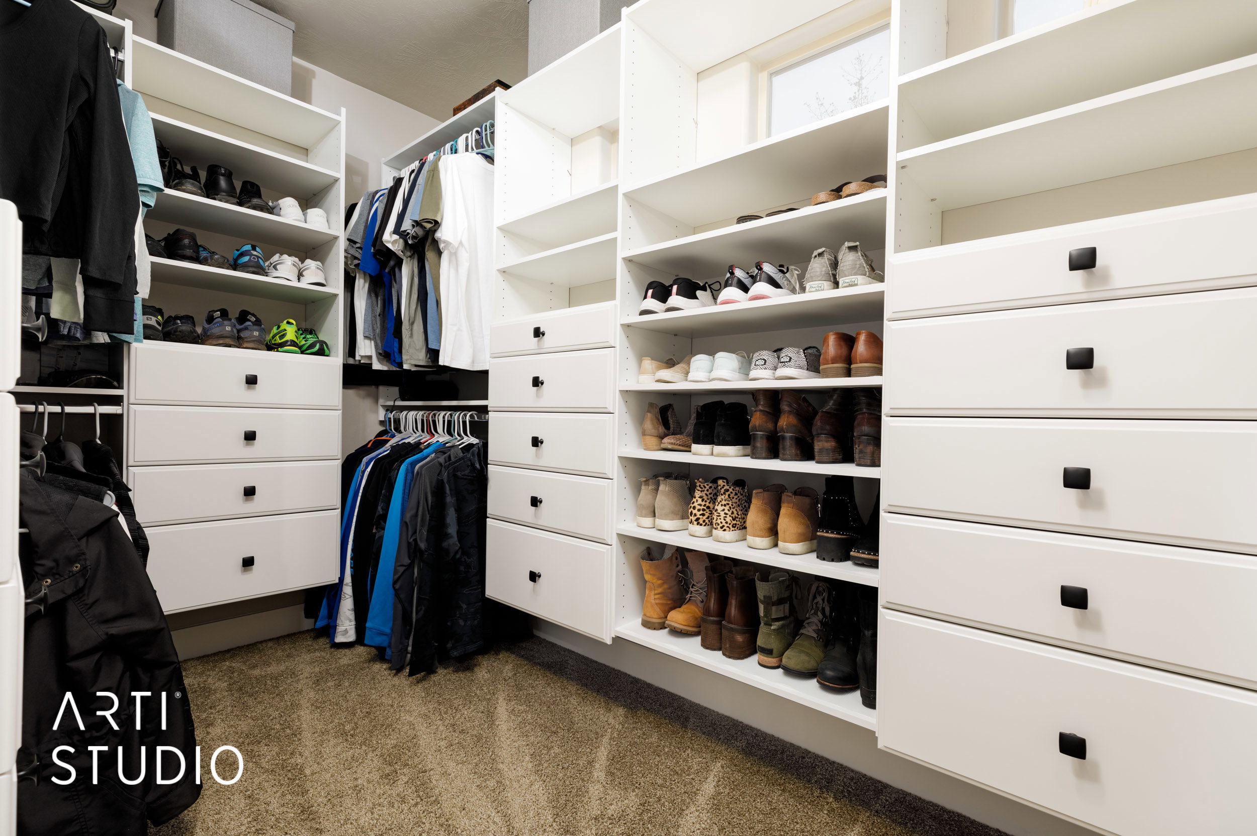 Custom closet organization system featuring white cabinetry with black hardware, extensive shelving, integrated drawer storage, and multiple hanging rods