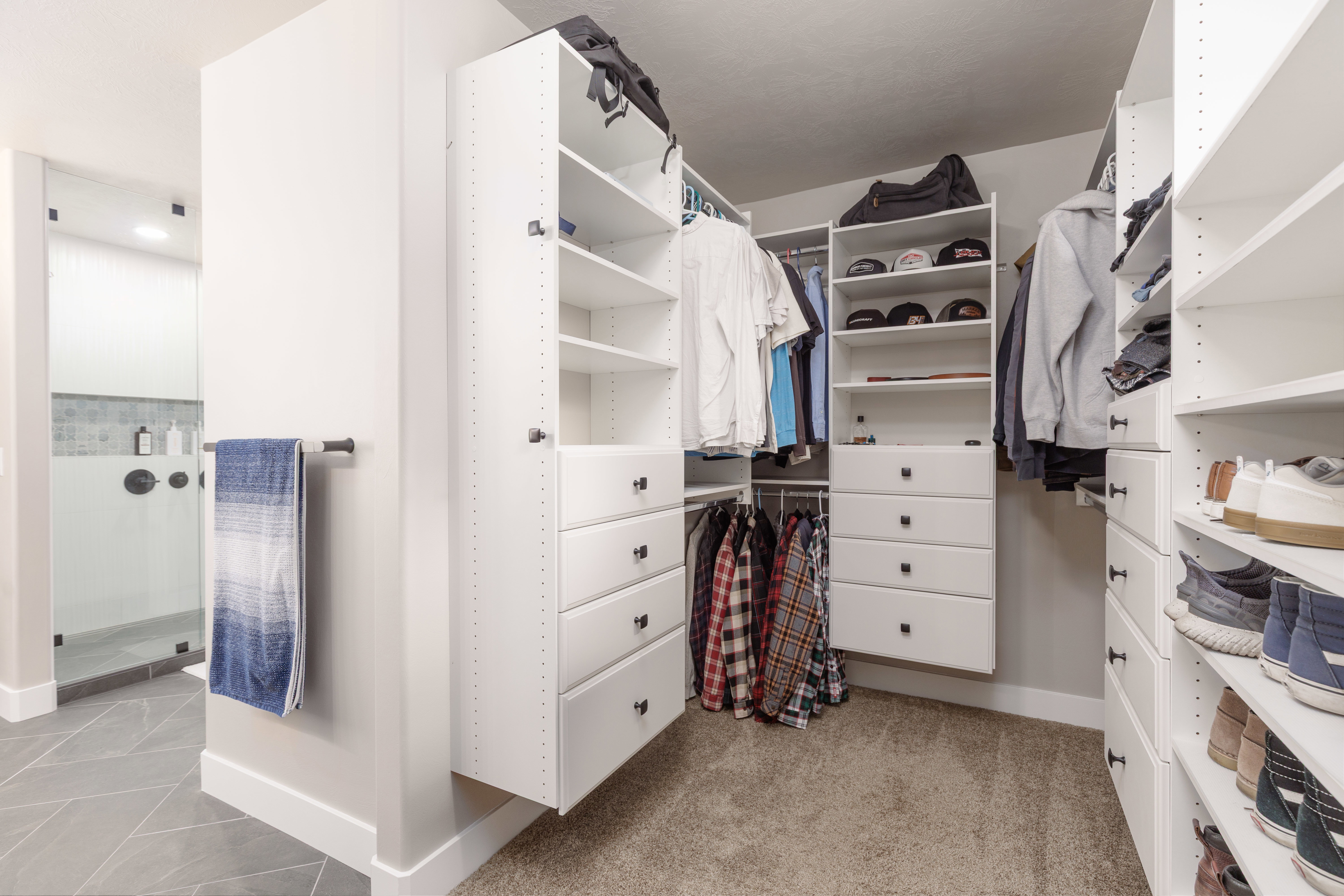 Custom closet organization system featuring white cabinetry with black hardware, extensive shelving, integrated drawer storage, and multiple hanging rods