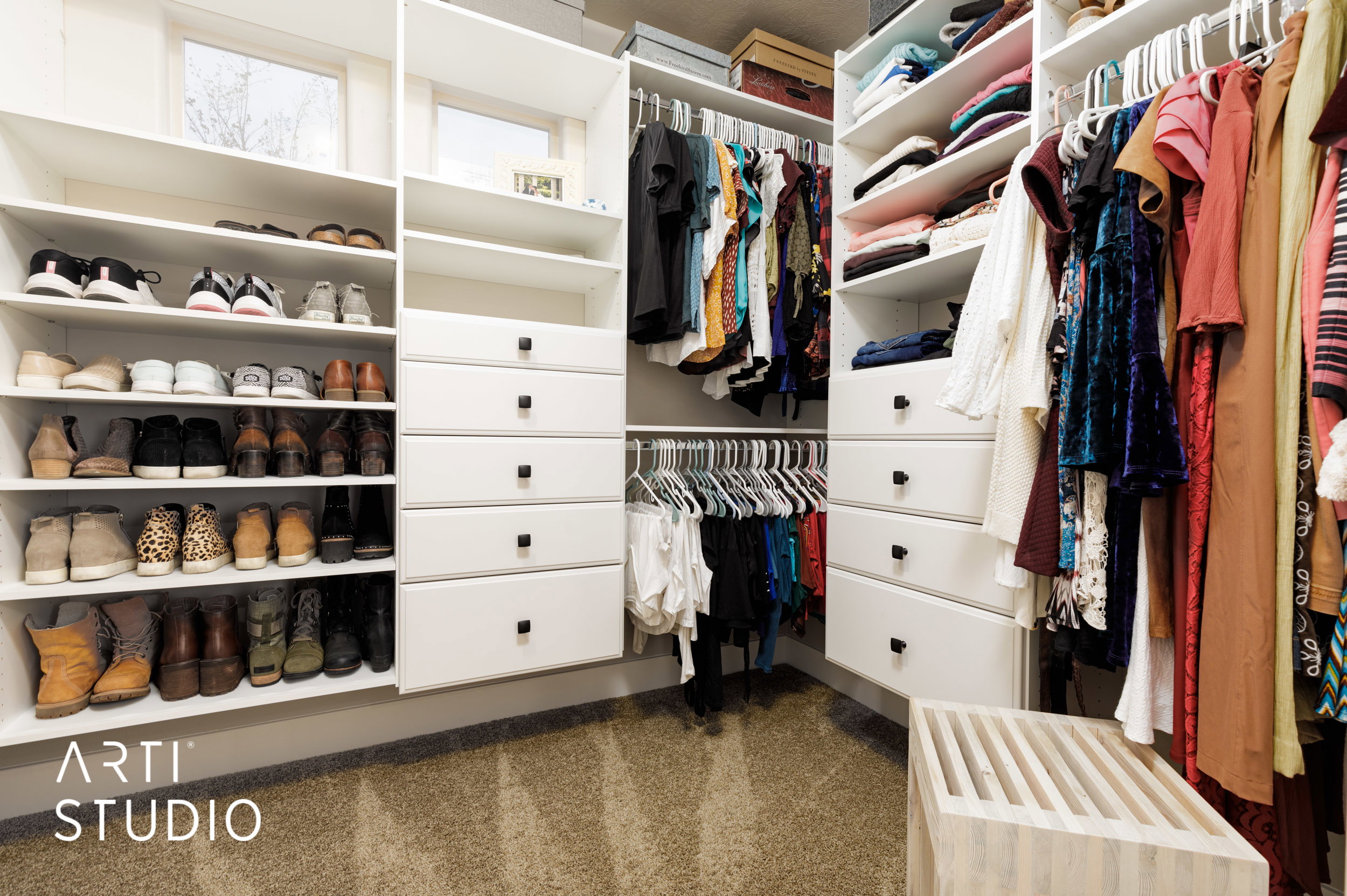 Custom closet system featuring extensive shelving, multiple hanging sections, built-in drawers with dark hardware, and natural light from transom windows