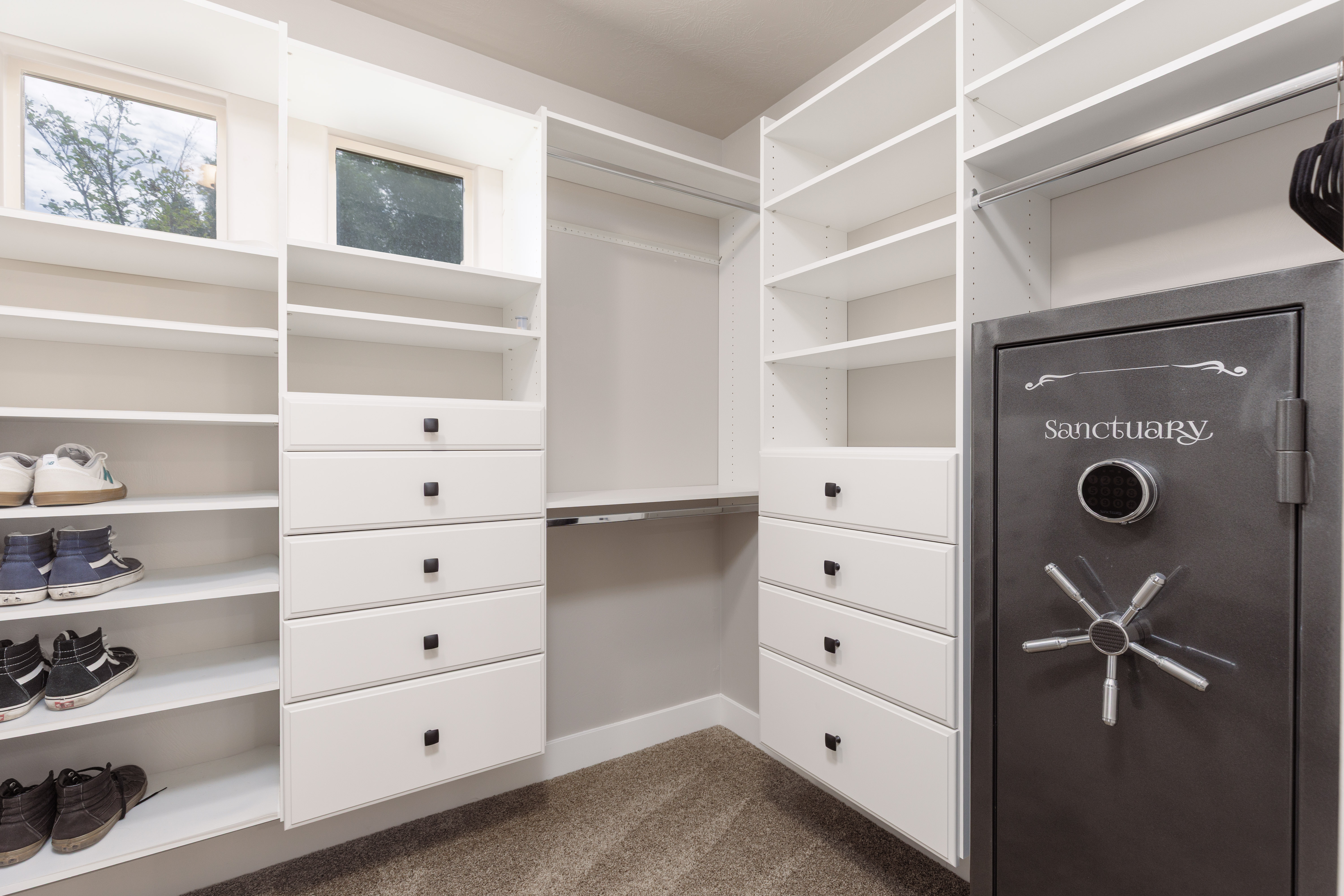 Custom closet system featuring extensive shelving, multiple hanging sections, built-in drawers with dark hardware, and natural light from transom windows