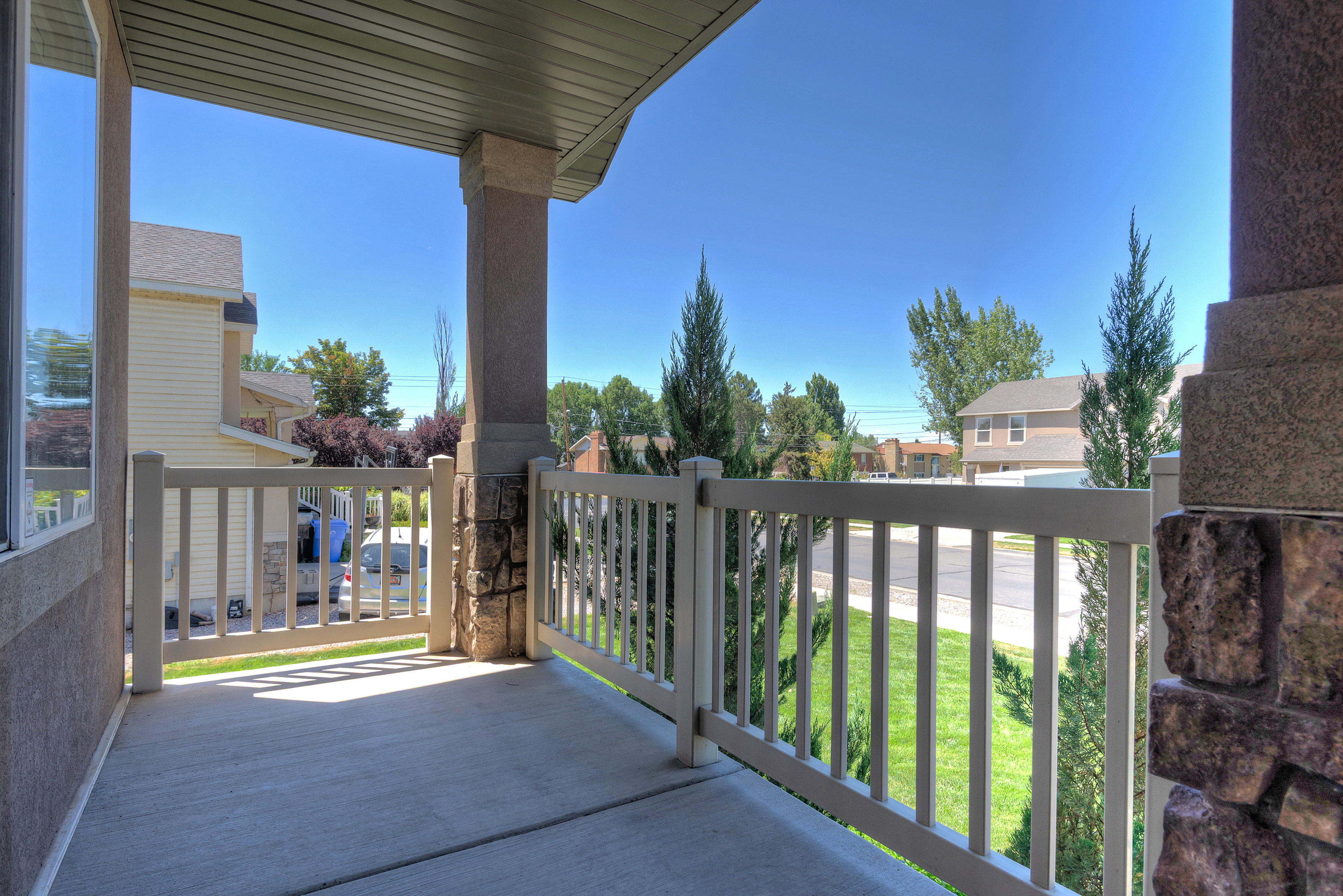 Covered porch featuring a concrete floor, light-colored railing, and stone-accented columns