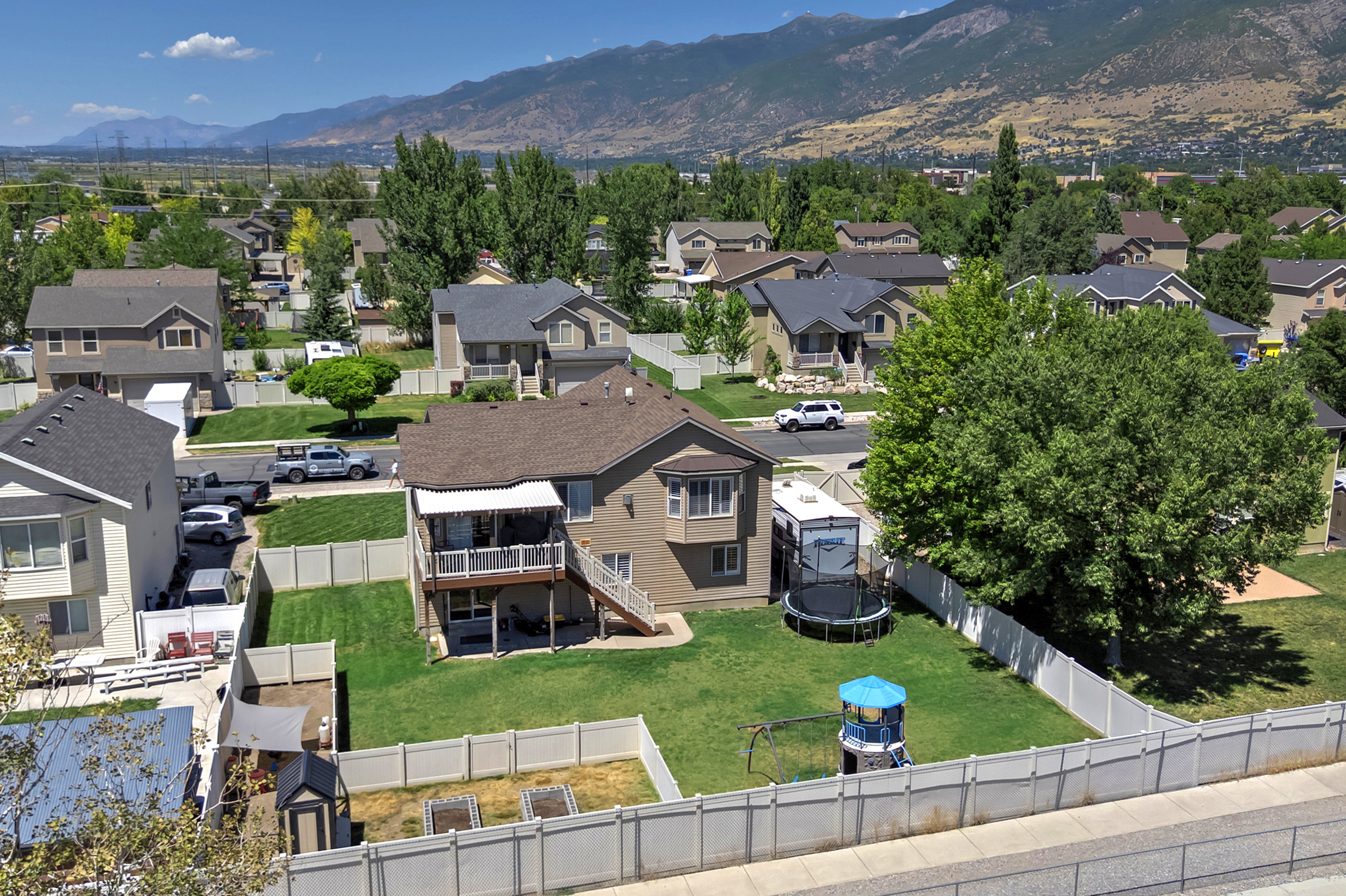 Expansive backyard featuring a green lawn, white vinyl fencing, and a covered second-story deck with stairs to the ground level