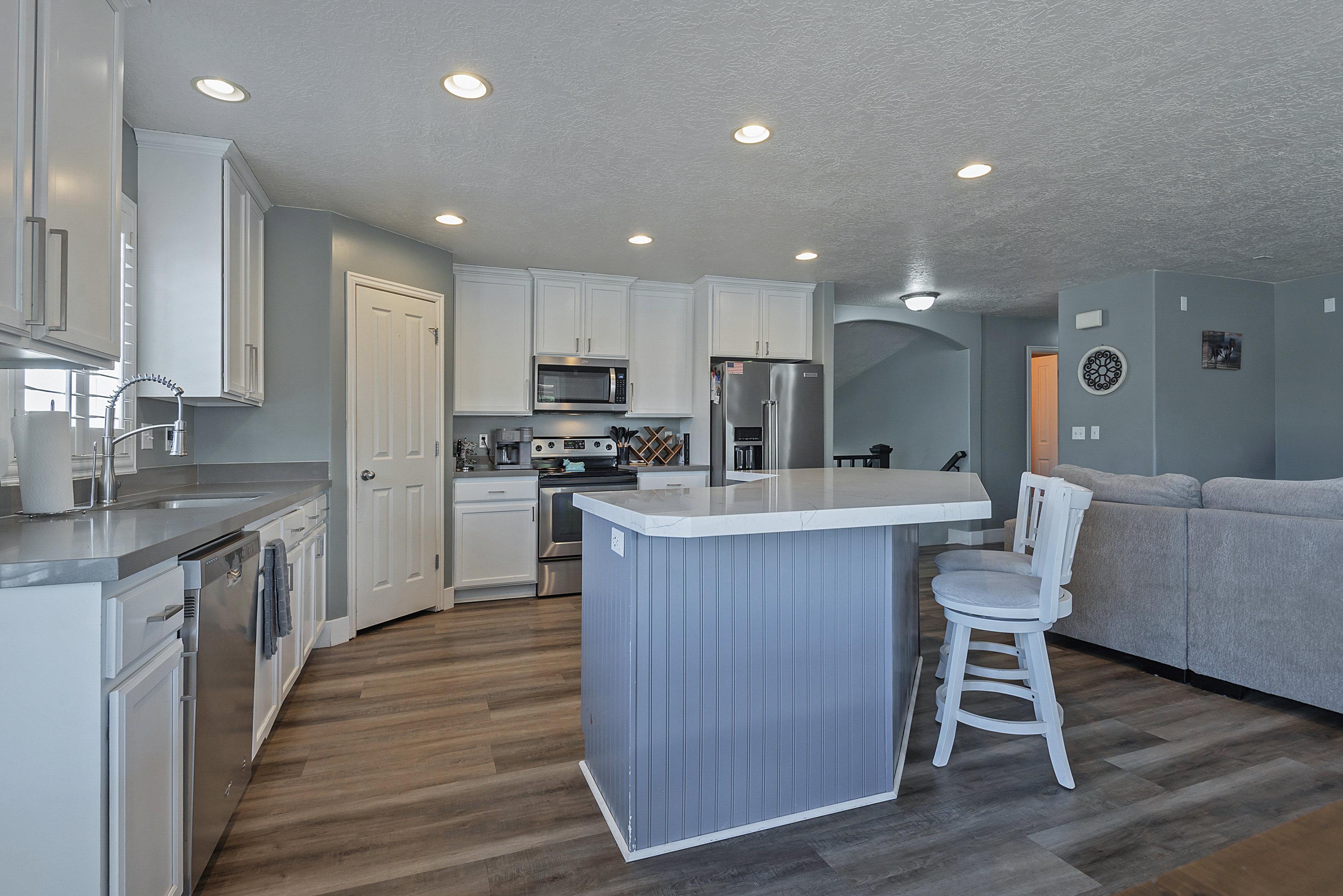 Kitchen featuring wood-finish flooring, recessed lighting, white cabinetry, a central island with beadboard paneling, and stainless steel appliances