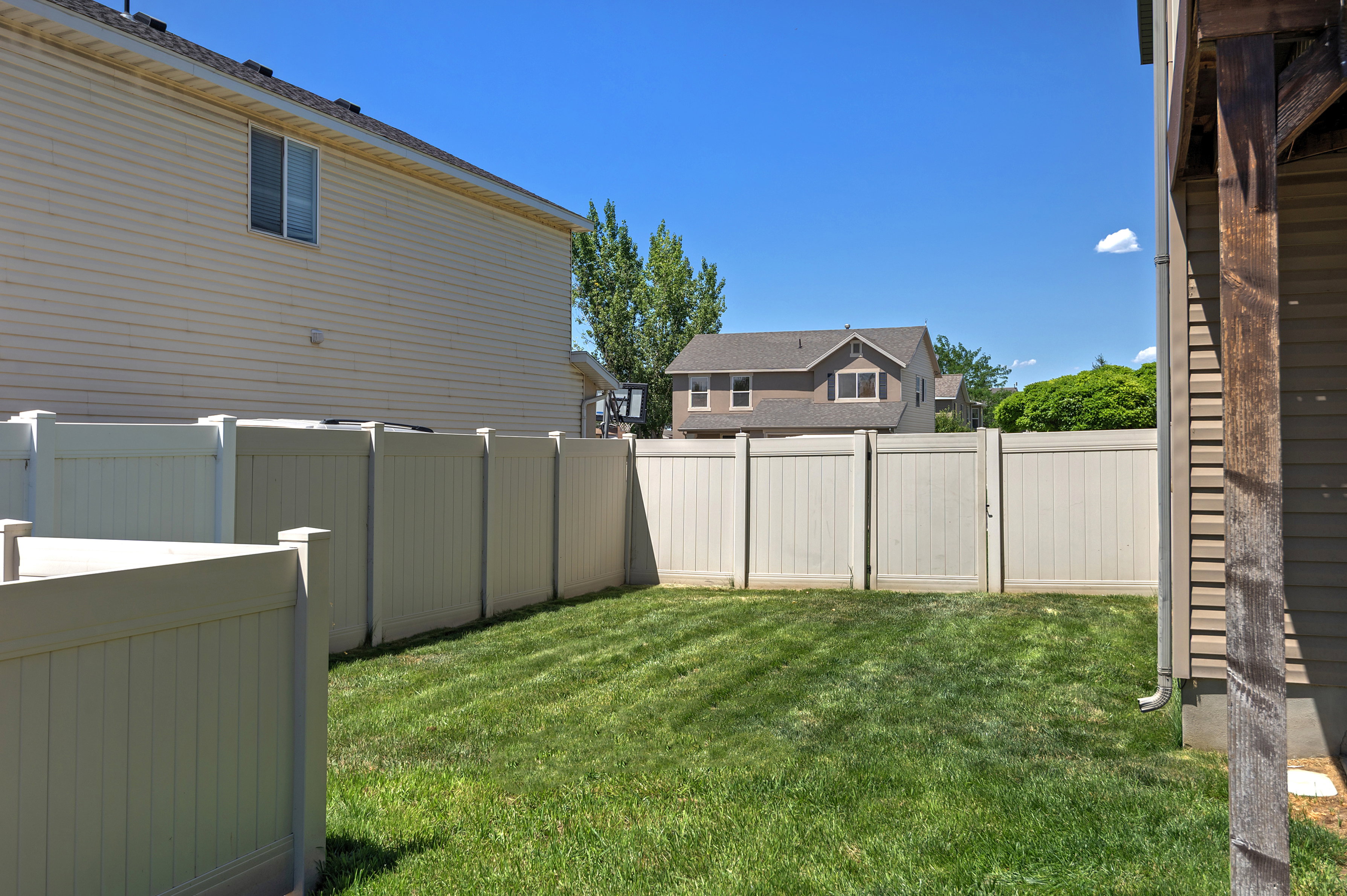 Fenced backyard with a manicured lawn, featuring a light-colored privacy fence and an external wood-finish column